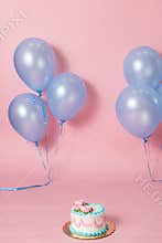 A pink backdrop with blue purple lavender balloons for a backdrop birthday celebration with a small birthday cake