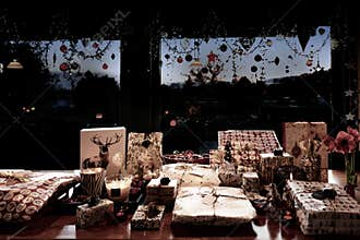 Christmas gifts before giving. Wrapped gifts are layed on table, in between candles and decorations. Decorated windows
