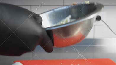 Male hand of cook in glove tossing ingredients and stirring them in iron bowl at kitchen. Arm of chef mixing chinese