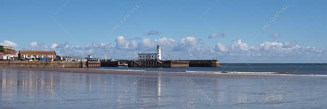 panoramic scenic view of Scarborough lighthouse and harbour reflected in the wet beach sand on a sunlit summer day