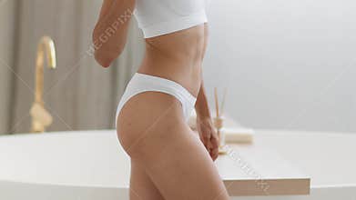 Unrecognizable slim woman in underwear caressing her soft silky skin with white feather at bathroom, free space