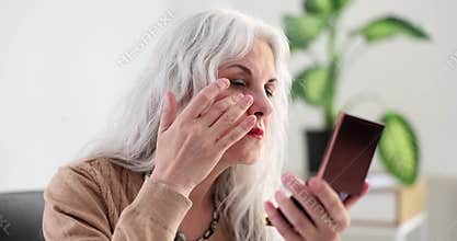 Elderly woman with gray hair looking at wrinkles and bags under eyes in mirror at home 4k movie slow motion