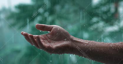 Cinematic shot of raindrops falling on man's hand during the raining on green nature on background. Male hand