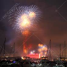 Brilliant fireworks over boats in harbor night scene