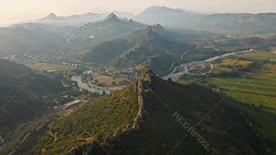 aerial scenic landscape with green fields, meadows, curved mountain river and mountain ridge with high mountains and