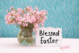 Blessed Easter - christian card with text and little pink flowers in vase on blue background