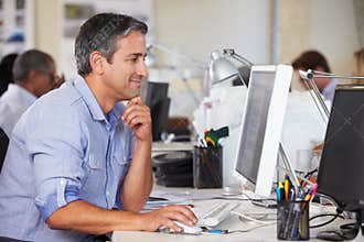 Man Working At Desk In Busy Creative Office