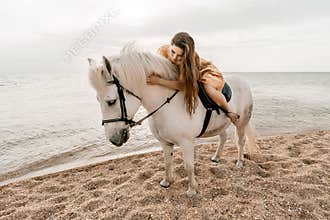 A white horse and a woman in a dress stand on a beach, with the sky and sea creating a picturesque backdrop for the