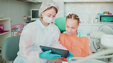 Woman dentist shows video on tablet to teen girl patient in dentistry.