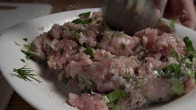 The girl mixes minced meat with chopped herbs and beaten fresh egg.