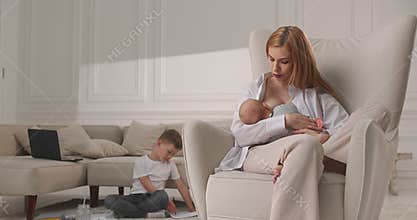 The mother lulls the child in the chair and the eldest son draws a picture of the mother.