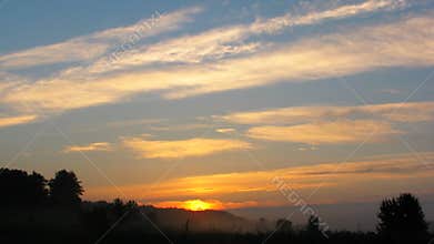 Dawn and sunrise over the field. Summer morning. Light clouds. Orange clouds in the blue sky. Timelapse
