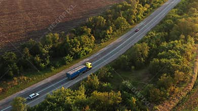 Aerial shot of a grain truck driving on the road in beautiful countryside in the summer sunset. Drone view of lorry
