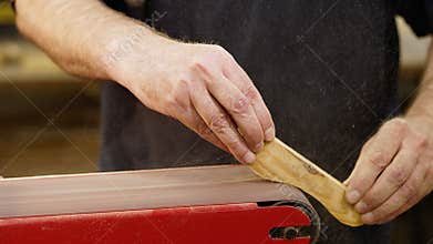 Hands of carpenter sharpens wooden part on grinding machine. Handwork concept, woodworking workshop.