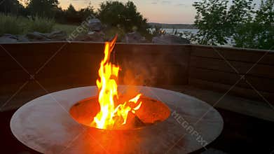 Bonfire burning in the forest in evening. Throwing log into the fire. Night bonfire, flames from fire, sparks fly.