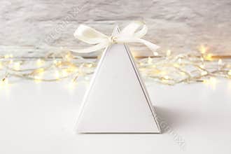 Blank white favor box with string of light and white wall background.