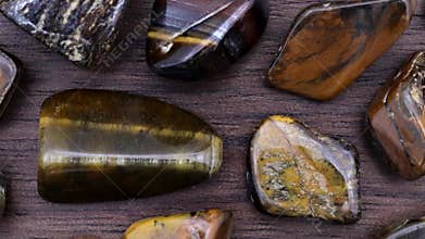 Tiger\'s Eye rare jewel on brown varnished wood texture. Sparse mineral pebbles background