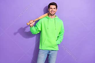 Photo of positive dangerous guy with brunet hairdo dressed green hoodie hold baseball bat on shoulder isolated on purple