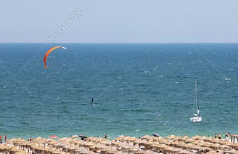 High angle shot of beach with straw canopies, sailboat, paraglider  on sea in mamaia, romania