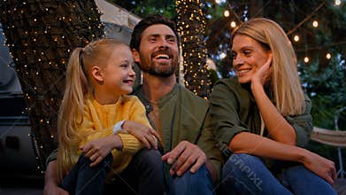 Caucasian family adult parents with child girl kid sitting in camping camp outdoors tourism trip hugging cuddling talk