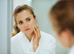 Woman in bathrobe checking her face in mirror