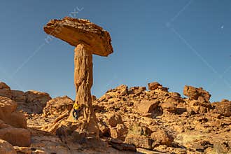 A tourist poses for the camera next to the base of “the mushroom”, a characteristic rock formation of Ennedi. Chad.