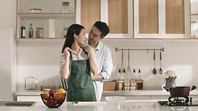 young asian man tying up apron for wife in kitchen at home