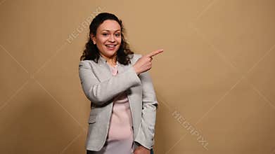 Happy positive woman laughing and pointing finger at a copy space for your ads on beige background