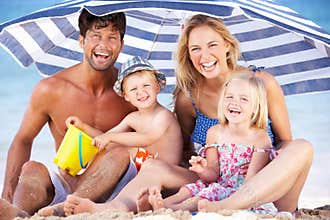 Family Sheltering From Sun Under Beach Umbrella