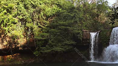Stunning Thai waterfall on Koh Kood island flows gracefully over rocky cliffs into serene pool, vibrant green