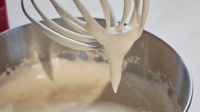 Close-up view of a kitchen mixer from which a beaten egg with sugar slowly flows