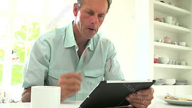 Middle Aged Man Looking At Digital Tablet Over Breakfast