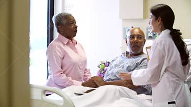 Female Doctor Talking To Senior Couple In Hospital Room