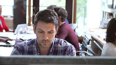 Architect Working At Desk With Meeting In Background