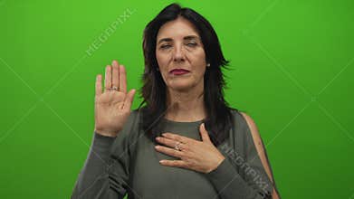 Hispanic middle age woman with raised palm and hand on chest in studio taking an oath gesture; commitment