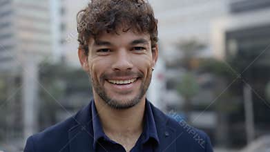 Portrait of joyful Hispanic businessman turns head to camera in city