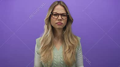 Blonde woman wearing glasses and green sweater vest furrows brow in purple studio set; frustration doubt