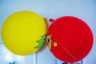 Close up view of red and yellow balloons with cartoon faces hanging on wall during birthday celebration.