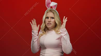 Woman with bunny ears making funny faces against a red backdrop, expressing surprise and humor, captures playful energy of a young