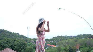 Young woman with floral dress enjoy looking landscape scenery and grab a hat while walk on hilltop terrace with sea view