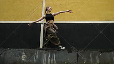 Attractive gen z young woman dancing contemporary dance against urban wall