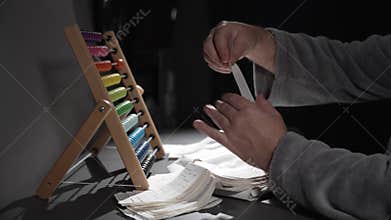 A man counts expenses on wooden abacus. The man is keeping records.