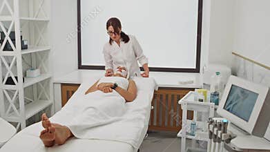 A beautician applies anesthesia to the face of an elderly woman.