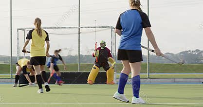 Female hockey players competing on field, focused on scoring goal