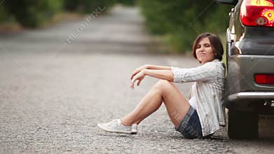 Sad pretty girl sitting on the road after car accident