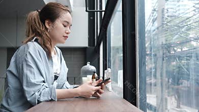 Focused Woman Using Smartphone near window in Modern Cafe