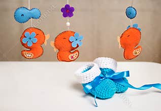 Blue knitted baby shoes with a blue ribbon around toys rattles.