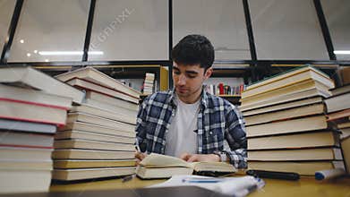Student studying diligently surrounded by stacks of books in a cozy library during daytime hours for academic success