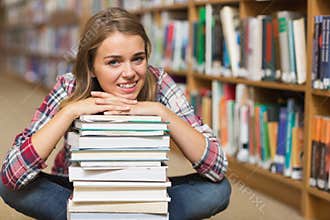 Smiling student sitting on library floor leaning on pile of books