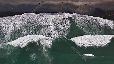 Aerial View of Surfers in Ocean Waves Crashing on Dark Sandy Beach